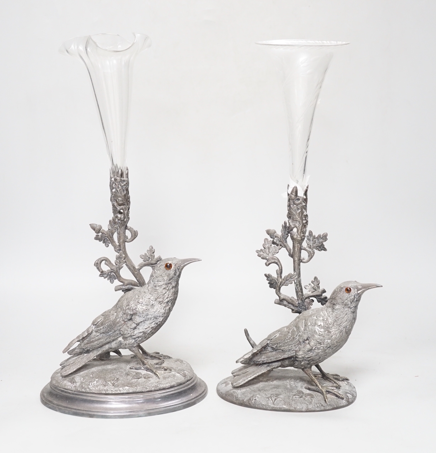 A matched pair of silver plated bird vases, with glass flutes, one with etched decoration, the largest 35cm high